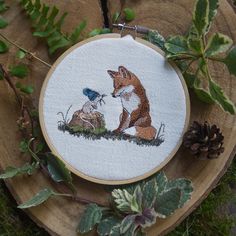 a fox and bird are sitting on the ground next to each other in a embroidery hoop