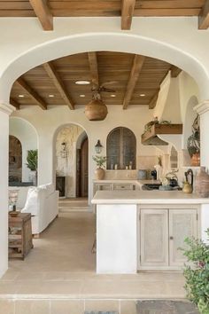 an archway leads to the kitchen and living room in this mediterranean style home, which is decorated with white furniture and natural wood accents