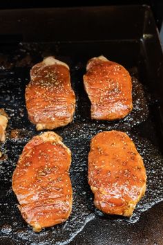 four pieces of meat are cooking in a black skillet on the stove with some seasoning sprinkles