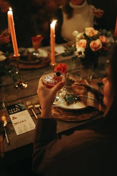 a woman holding up a drink in front of a table full of people and candles