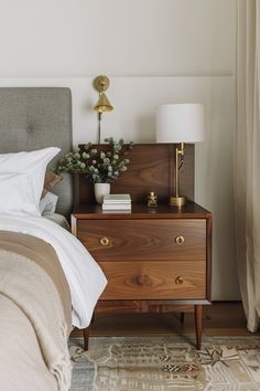 a bedroom with a bed, nightstand and lamp on top of the night stand in front of the window