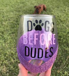 a hand holding up a wine glass with the words dogs before dudes written on it