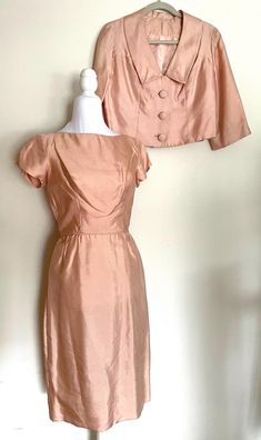 This beautiful little pink silk suit is made with a fitted short sleeved dress and jacket with 3/4 sleeves and covered buttons. The vintage dress closes with a metal zipper. It is made of high quality silk and is in excellent vintage condition.  This is one of the best, most wearable 50s dress suits around. Rare in Medium size.  Approximate Measurements: Dress Bust 37" Waist 26" Hips 36" Length 40" Jacket Bust 38" Waist 34" Sleeve length 16" Please measure carefully for the perfect fit.  As always, SwingDecades provides free shipping for orders of $35 or more to the Continental United States.  Thank you for shopping SwingDecades and favorite the shop to stay current with new listings as the shop grows Shop policy and Information: All measurements are taken with the garment flat, doubled fo Fitted Evening Sets With Short Sleeves, Elegant Fitted Short Sleeve Set, Fitted Silk Feminine Set, Fitted Silk Skirt Suit For Evening, Feminine Fitted Silk Set, Pink Skirt Suit For Formal Spring Occasions, Fitted Short Sleeve Sets For Party, Pink Silk Evening Set, Elegant Pink Skirt Suit For Party