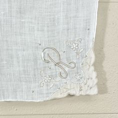 an embroidered monogram on the side of a white linen piece with silver thread and sequins