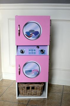 a pink toy oven sitting on top of a tiled floor next to a basket filled with laundry