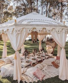 a white canopy bed sitting on top of a lush green park covered in pillows and blankets