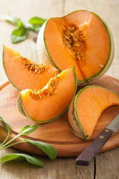 two pieces of melon on a wooden cutting board with a knife and green leaves