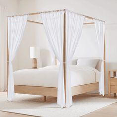 a canopy bed with white drapes on the top and bottom posts, in a bedroom