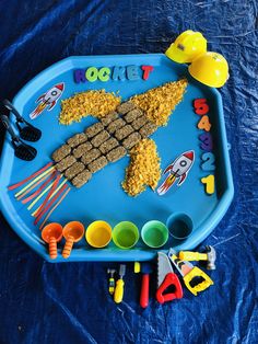 a blue tray filled with food on top of a blue tablecloth covered floor next to toys