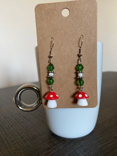 Adorable and trendy handmade mushroom drop earrings! Made with cute Fairycore mushroom charms paired with green beads. Simple and tasteful!  * All materials were cleaned and sanitized prior to use and kept in a clean smoke free environment. Comes packaged in a mesh bag. Whimsical Green Jewelry With Mushroom Design, Green Mushroom Design Dangle Earrings, Green Dangle Earrings With Mushroom Design, Adjustable Green Mushroom Design Earrings, Green Adjustable Mushroom Design Earrings, Adjustable Green Earrings With Mushroom Design, Whimsical Green Mushroom Earrings, Whimsical Green Mushroom Design Earrings, Fairycore Mushroom