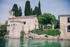 an old building sitting on the side of a lake next to trees and buildings in the background