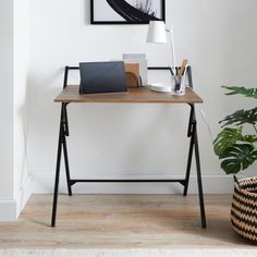 a laptop computer sitting on top of a wooden desk next to a potted plant