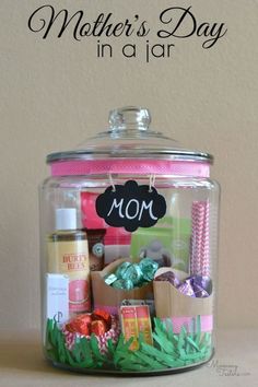 a glass jar filled with lots of different items on top of a wooden table next to a sign that says mother's day in a jar