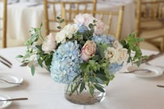 a vase filled with blue and pink flowers on top of a white table cloth covered table