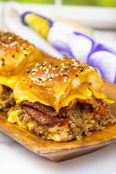 two sandwiches with meat, cheese and other toppings on a wooden plate next to an egg roll