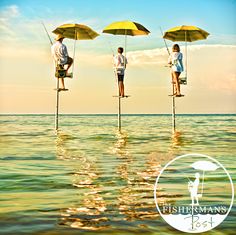 three people standing on stilts in the water with umbrellas over their heads and holding fishing rods