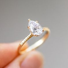 a person holding a gold ring with a pear shaped diamond in it's center