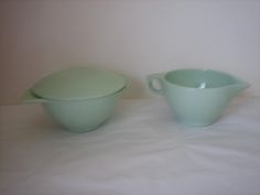 two green dishes sitting on top of a white tablecloth covered bed next to each other