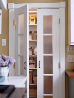 an open pantry door in a kitchen with baskets on the floor and shelves behind it