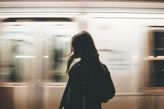 a woman standing in front of a train at a station with her back to the camera