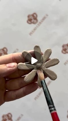 a person holding a paintbrush in their hand with a fake flower on top of it