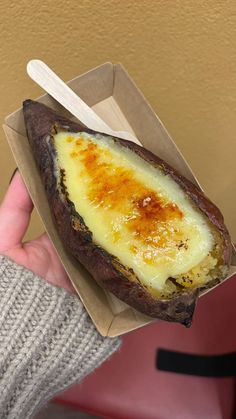 a person holding up a baked potato in a paper container with a spoon inside it