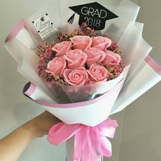 a hand holding a bouquet of pink roses in front of a graduation cap on top of a sign