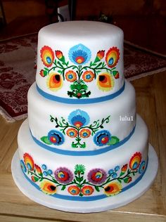 three tiered cake decorated with colorful flowers on top of a wooden table next to a rug