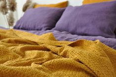 an unmade bed with purple and yellow sheets