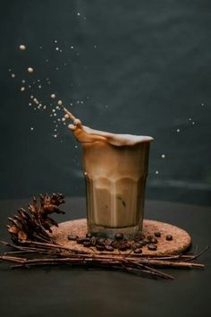 a glass filled with liquid sitting on top of a wooden table next to pine cones