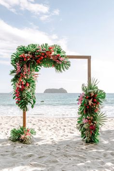 a tropical wedding arch on the beach with flowers and greenery for an outdoor ceremony