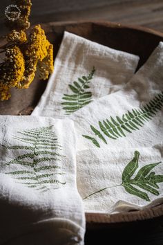 three white towels with green leaves on them in a wooden bowl next to dried flowers