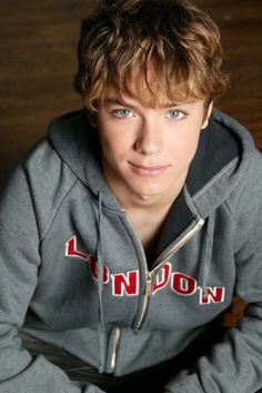 a young man sitting on top of a wooden floor wearing a gray sweatshirt and jeans