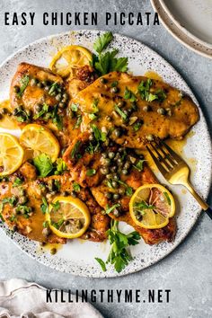 a white plate topped with chicken covered in sauce and garnished with lemons