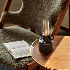 a table with a lamp on top of it next to a chair and an open book