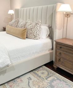 a bed with white sheets and pillows in a bedroom next to a lamp on a dresser