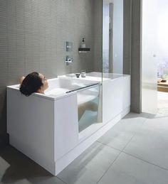 a woman laying down in a bathtub next to a sink and shower head mounted on the wall