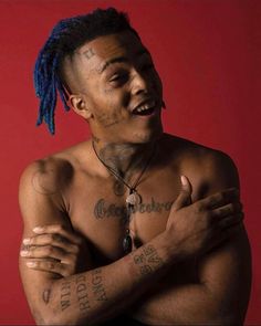 a shirtless man with blue dreadlocks and tattoos on his chest posing for the camera