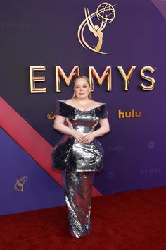 a woman in a silver and black dress on the red carpet at an awards event