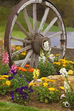 an old wagon wheel surrounded by flowers and rocks