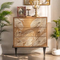 a gold leafy chest of drawers in a room with potted plants and pictures on the wall