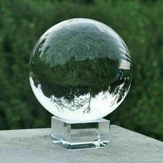 a clear glass ball sitting on top of a cement block next to some green trees