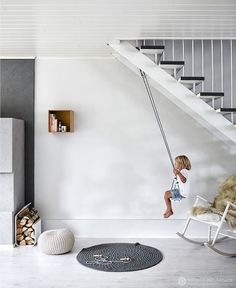 an image of a child swinging on a swing chair in the living room with stairs and bookshelves