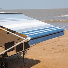 a camper trailer parked on the beach next to the ocean with its awning open