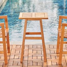 two wooden chairs sitting next to each other near a swimming pool with water in the background