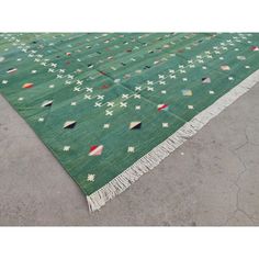 a green rug with white, red, and blue designs on the top is laying on concrete