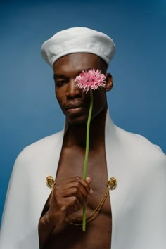 a man holding a pink flower in his right hand and wearing a white sailor's hat