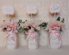 three mason jars with pink flowers in them on a shelf next to a brick wall