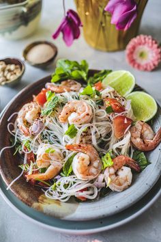 a plate with noodles, shrimp and vegetables on it next to some other food items