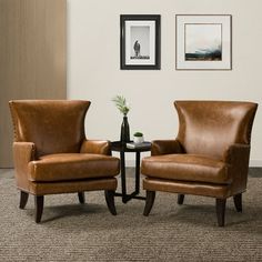 two brown leather chairs sitting next to each other in a room with pictures on the wall